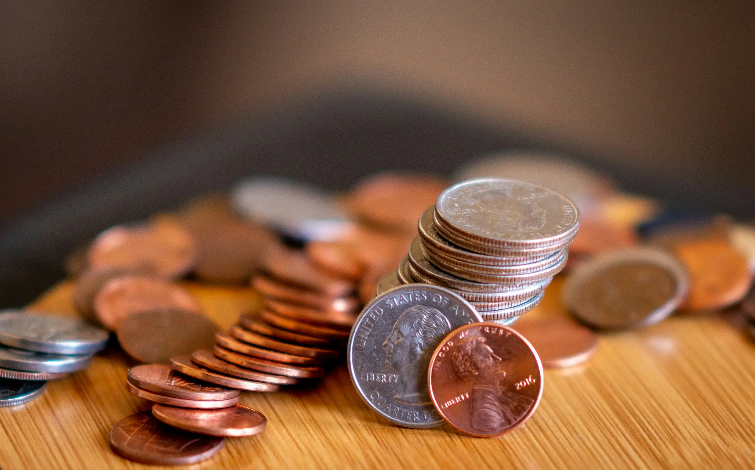 Loose copper and silver coins, some stacked, spread across a wooden table top.