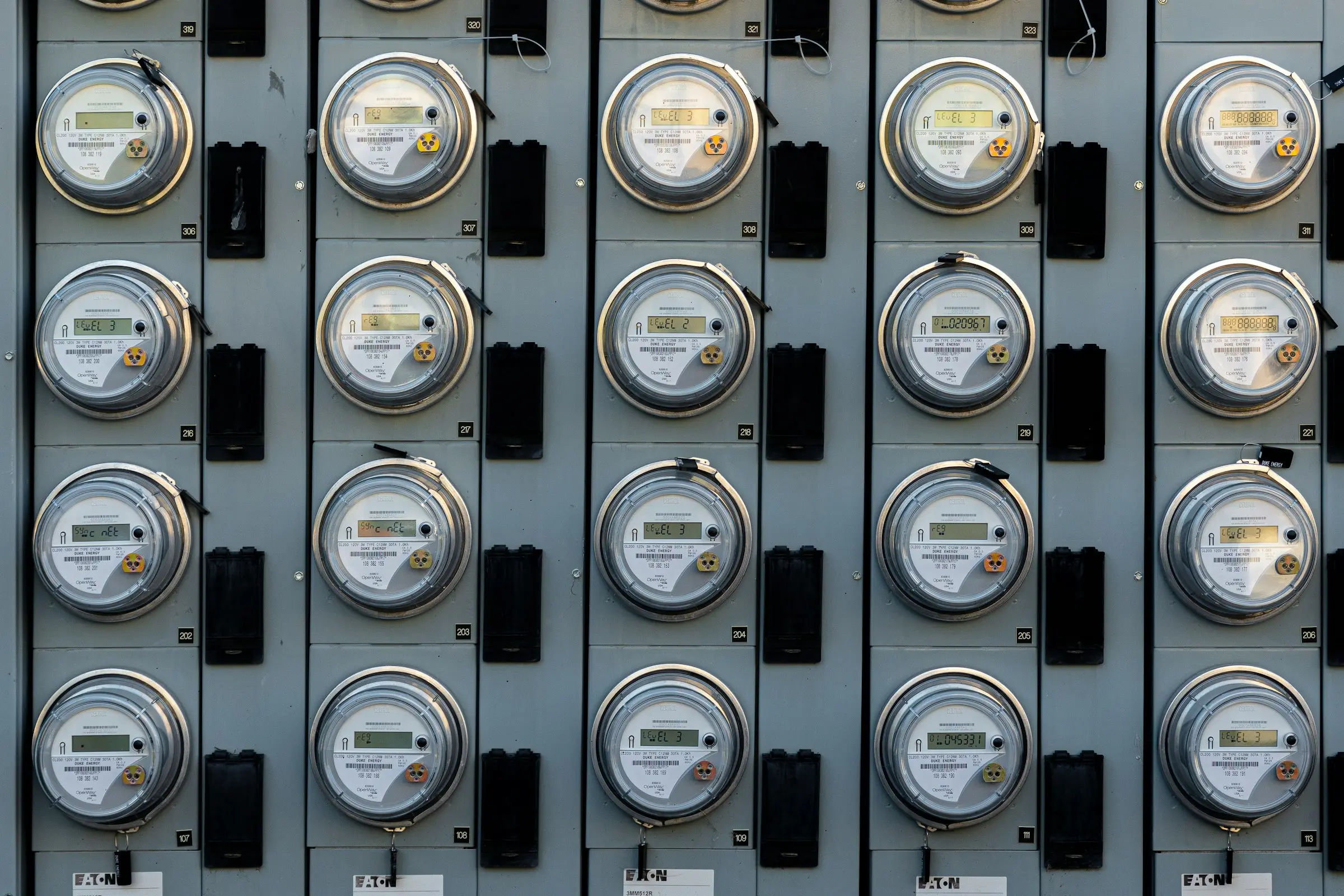 A wall of round electricity meters arranged in a grid of rows and columns on grey metal panels.