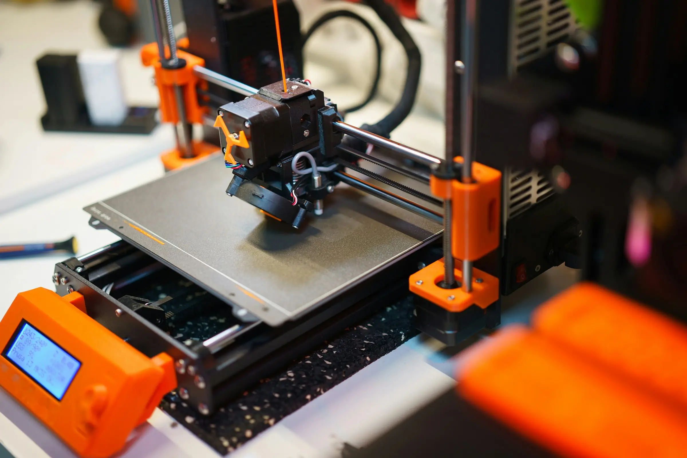High-angle view of an orange and black open-frame desktop 3D printer at work, with its control box beside it.